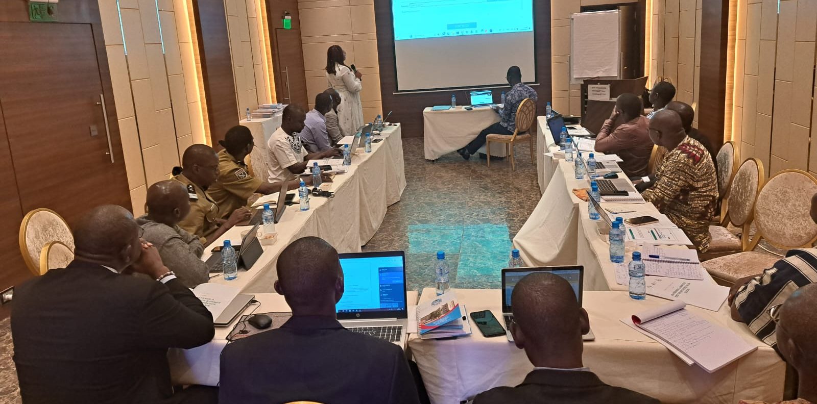 Participants seated at a U-shaped table of laptops and notebooks during an M&2N export training workshop in Ouagadougou, facing a projected screen.