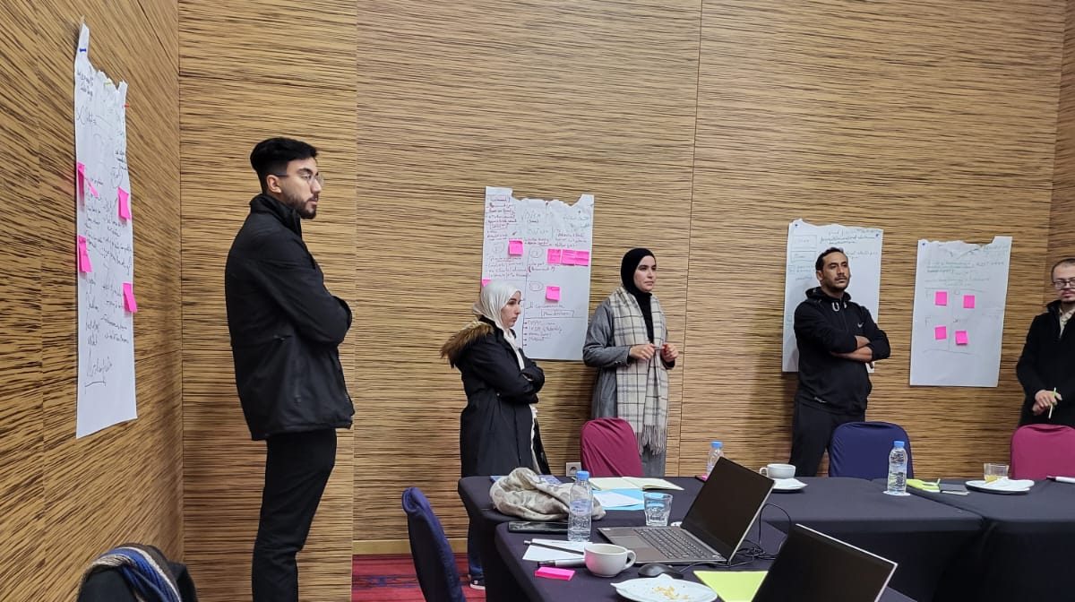 Participants standing beside flipcharts covered in sticky notes during a working session.